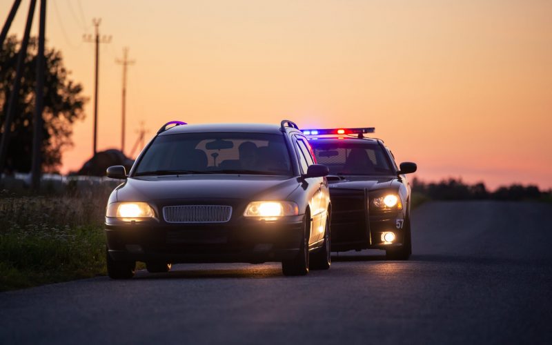 Speeding Driver Gets Pulled Over By Police Patrolling Car . Wide Shot of the Two Cars Stopped in a Road Crossing an Open Field. Drunk Driver Gets Caught by Professional Officers